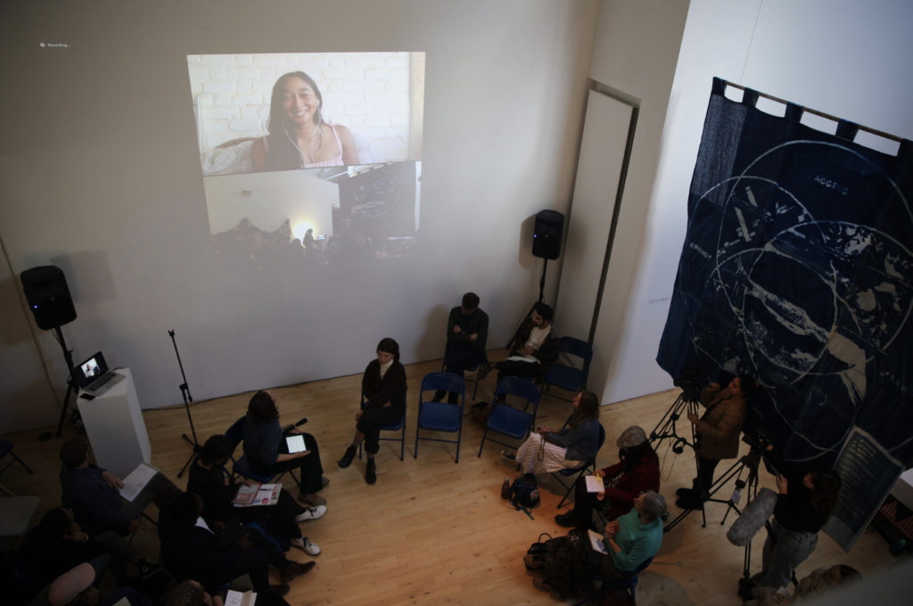 People sit looking at a person on the screen in a gallery.