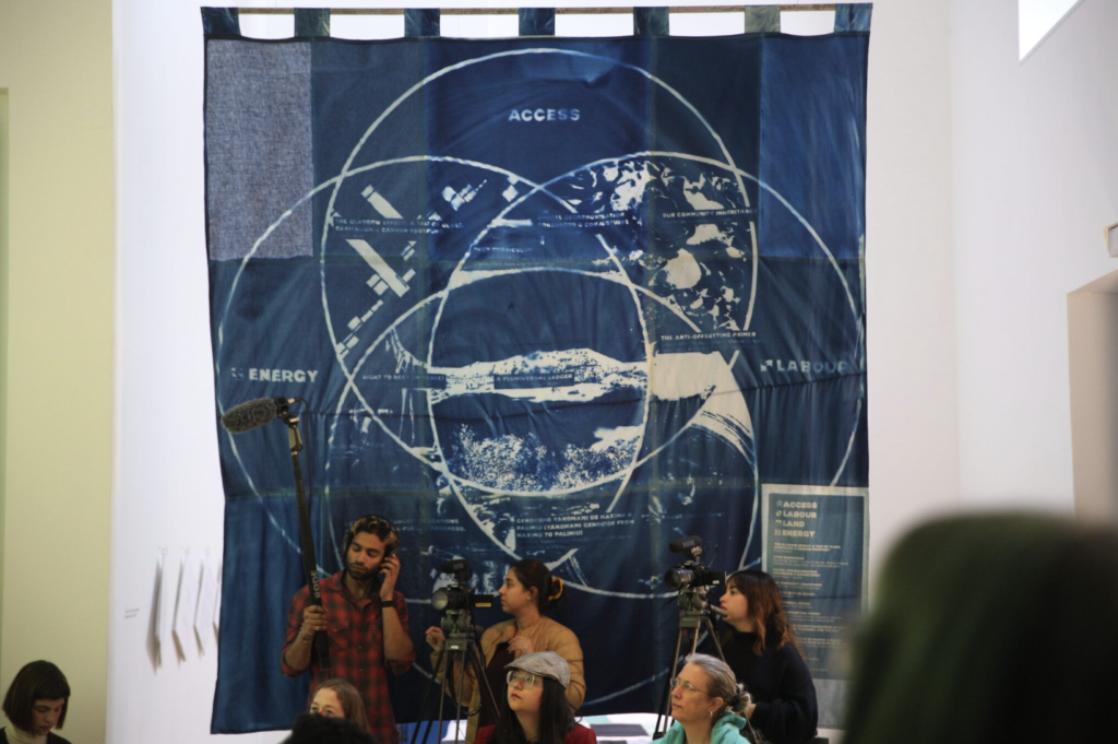 A large blue sheet of fabric with white circles and patterns. In front stands a camera crew in Stanley Picker Gallery.